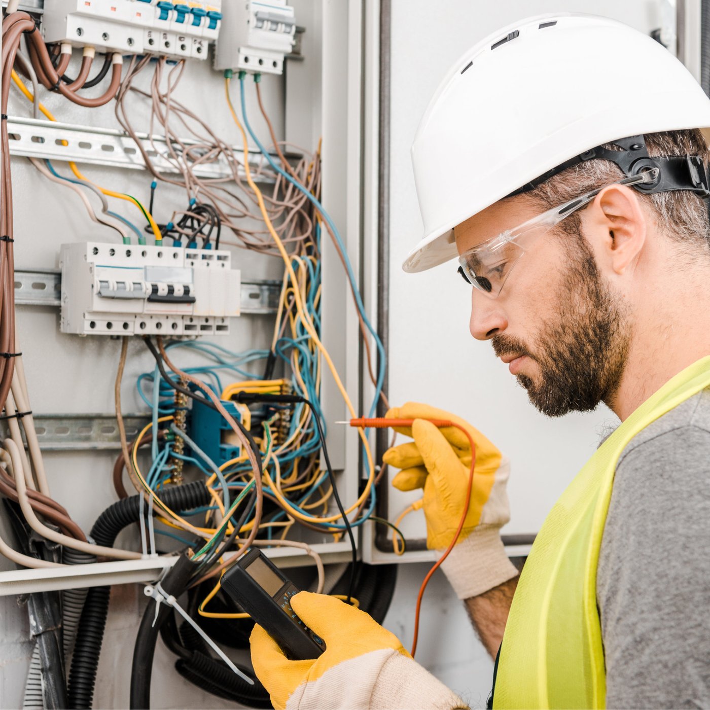Electrician in a hard hat testing circuits in an electrical panel
